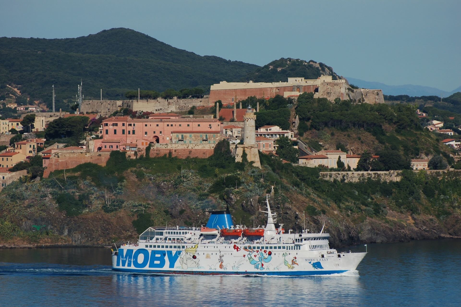 Traghetto Moby che naviga vicino all’Isola d’Elba, con le fortificazioni di Portoferraio sullo sfondo.